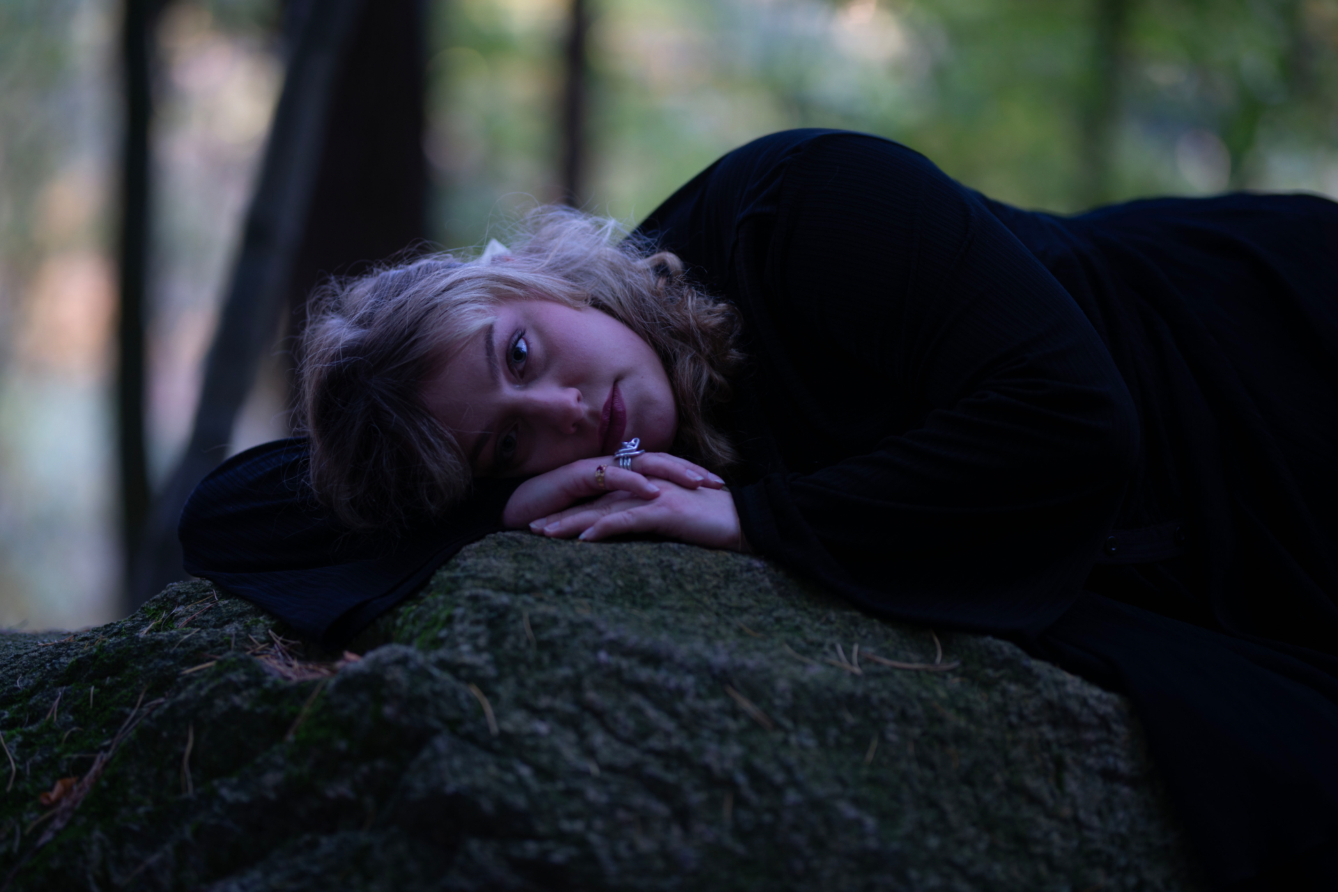 Woman resting on a mossy stone in a dusky forest