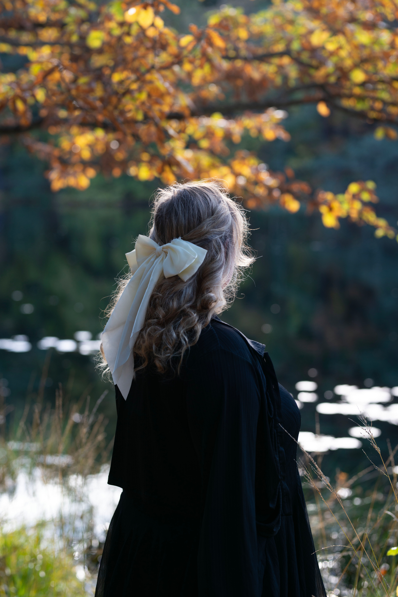 Woman with a cream silk bow looking out over an autumn lake